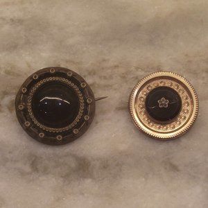 Two black and gold pins, one cracked